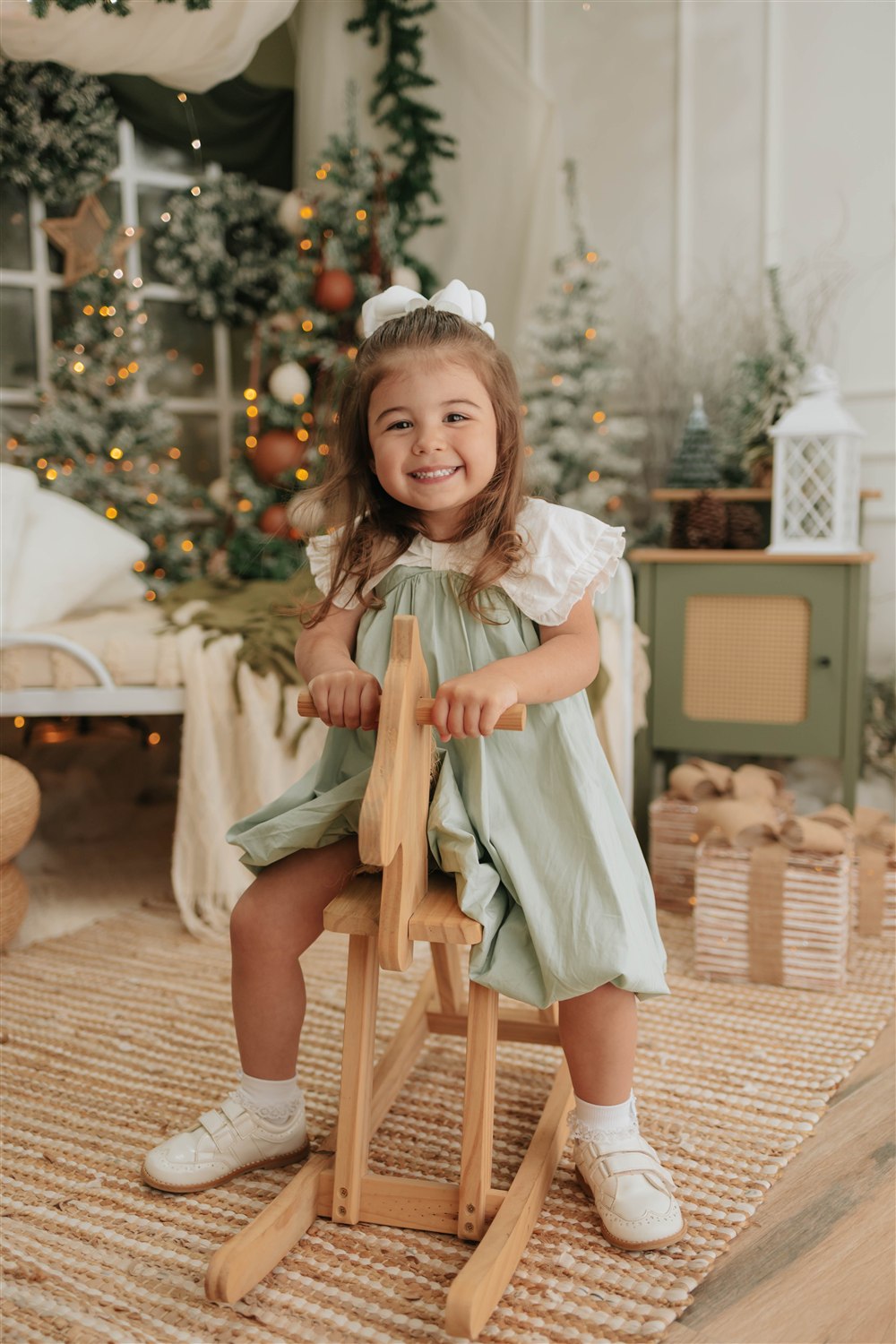 Menina sorrindo em um cavalinho de madeira ao lado da árvore de Natal